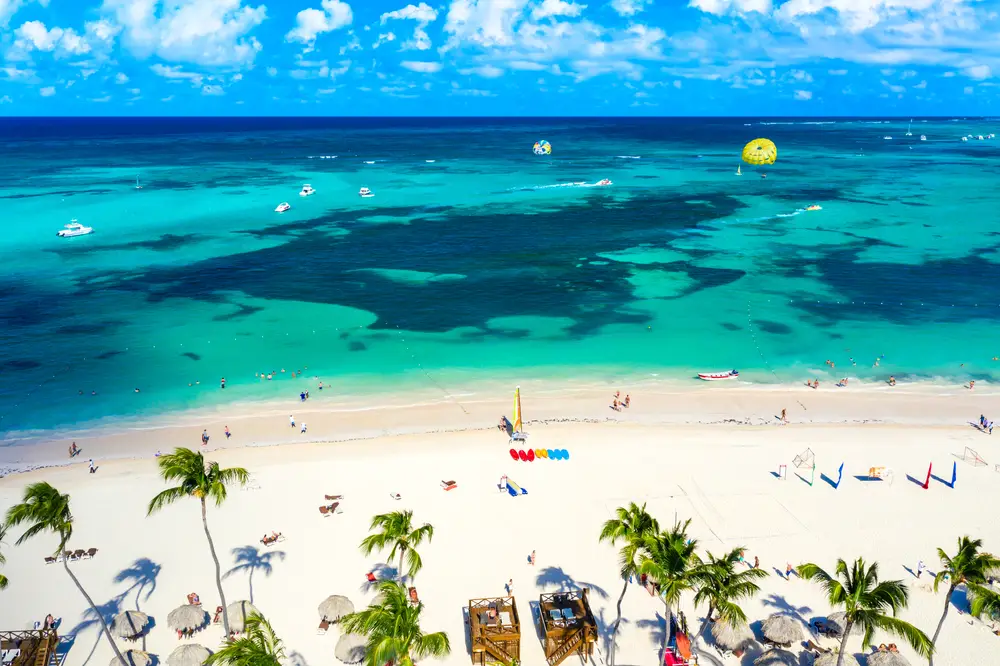 Aerial view of Bavaro Beach in the Dominican Republic with parasailing, beach chairs, and blue skies for a Puerto Rico vs the Dominican Republic comparison