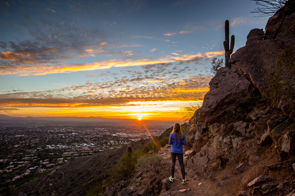 Woman watching the sun rise from the top of a mountain for a guide to the best areas to stay in Phoenix