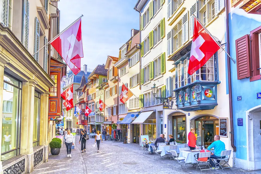 People walking around the city center of Zurich with little shops on either side of the cobblestone street during the best time to visit Zurich
