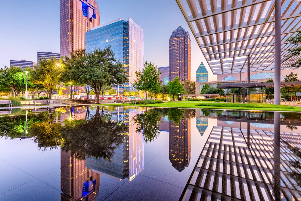 Downtown skyline and plaza in Dallas, TX in the afternoon with reflections on the water indicating this as one of the 5 cheap places to travel within the US