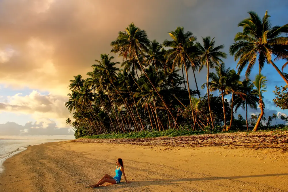 Young woman sitting on the beach at dusk on Taveuni Island in Fiji for a guide to what it costs to go there