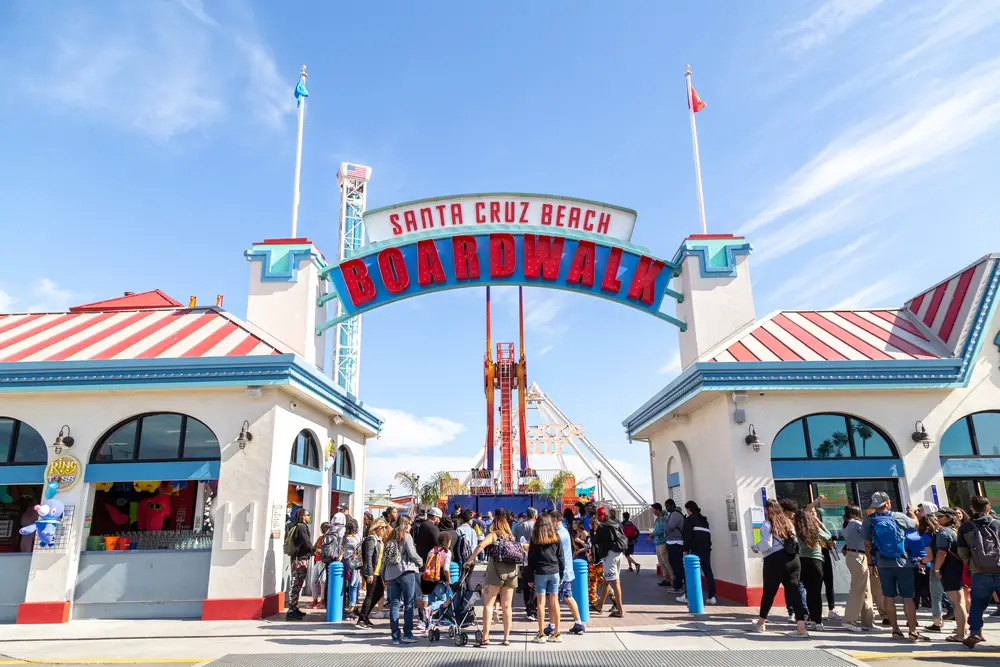 Photo of the entrance to the Boardwalk, one of the best places to stay in Santa Cruz, on a nice summer day with people gathering between the ticketing offices