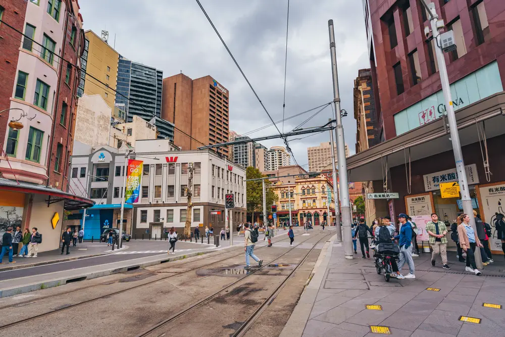 Busy day in one of the best parts of Sydney to stay, Chinatown, with people walking around the city above the trolley tracks between buildings on a semi-gloomy day
