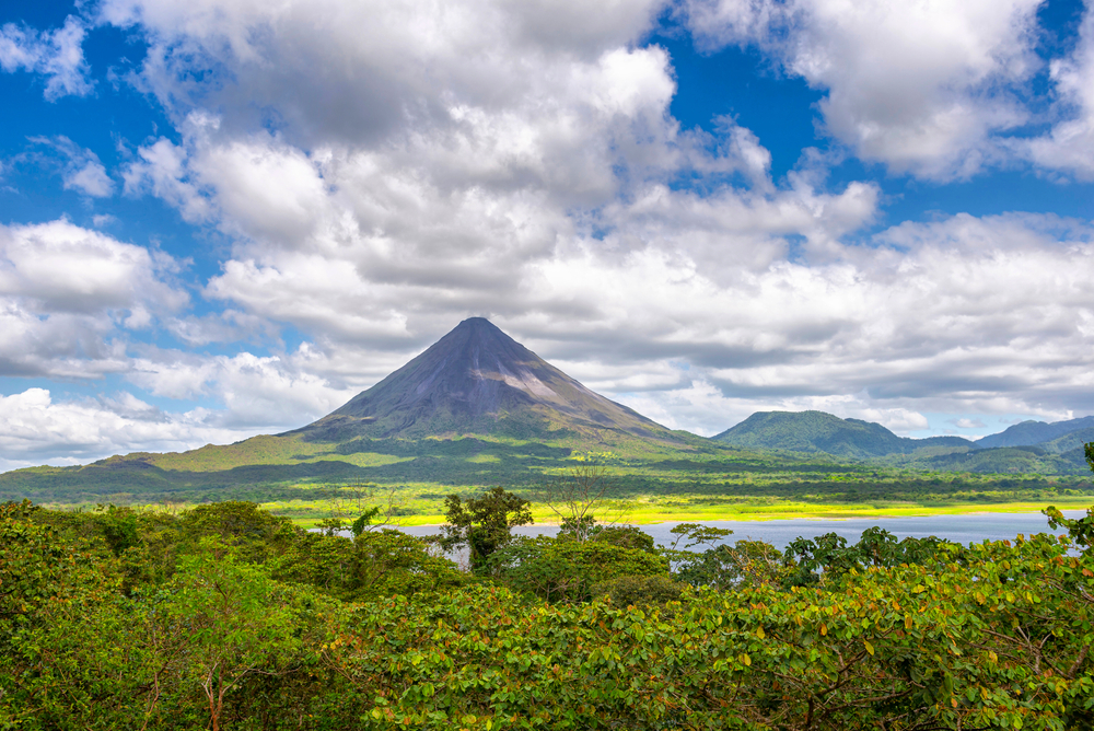 Wide view of the Arenal volcano in La Fortuna, Costa Rica with clouds overhead and green forests surrounding it for a list ranking the top trips for friend groups