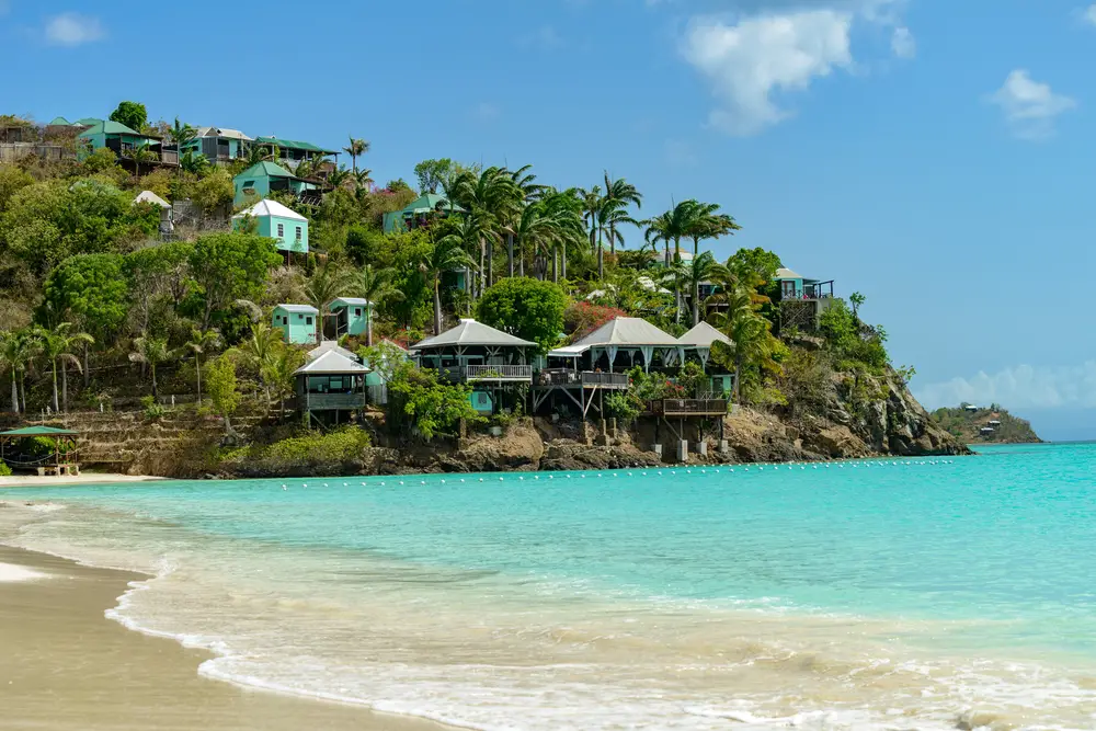 Beach at Jolly Harbour, Antigua with colorful houses on the water's edge on a clear day for a list of the top places to visit with a group of friends