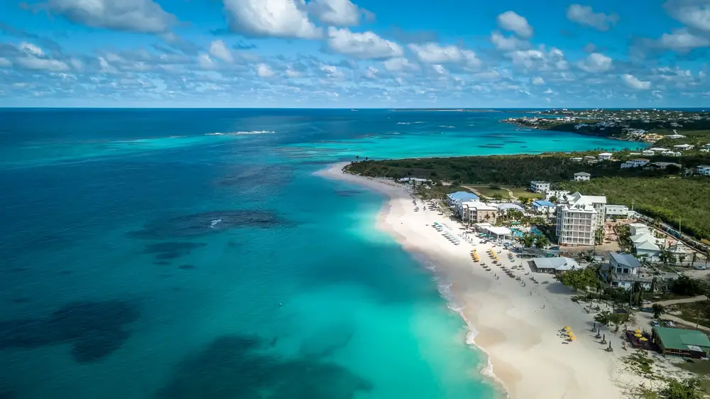 Aerial view on a beach with a few hotels on its shores and fine sand and clear emerald water. 