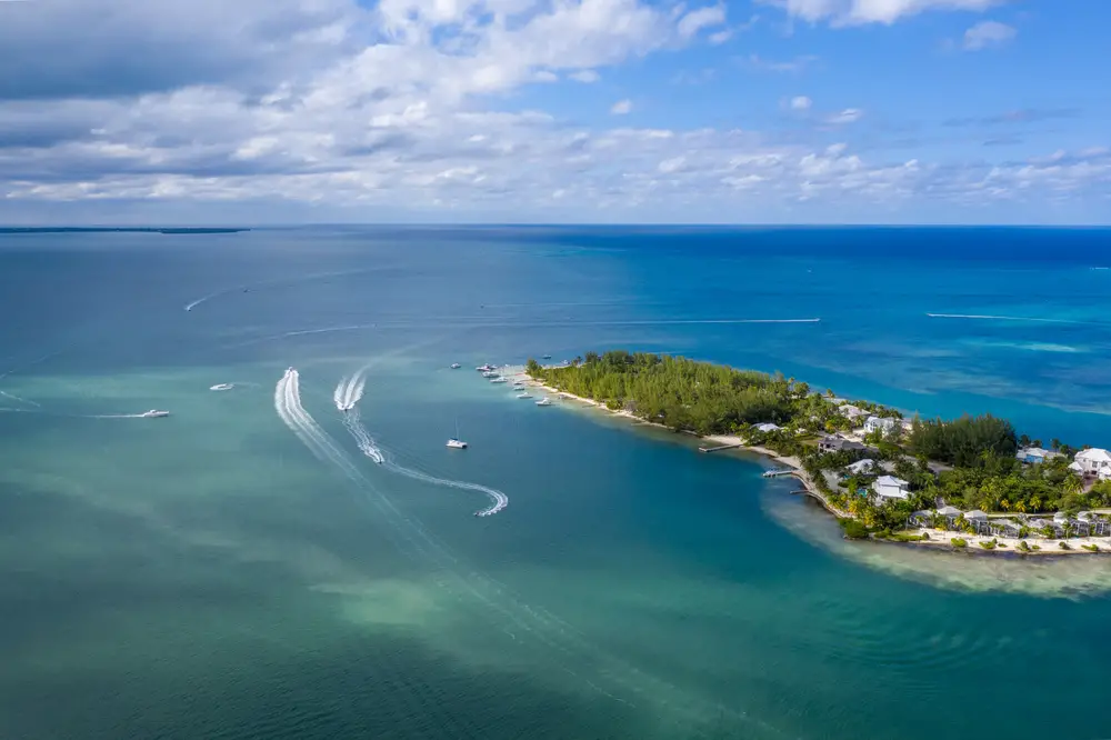 Aerial view on an island with resorts near its shore, and boats sailing on its deeper waters. 