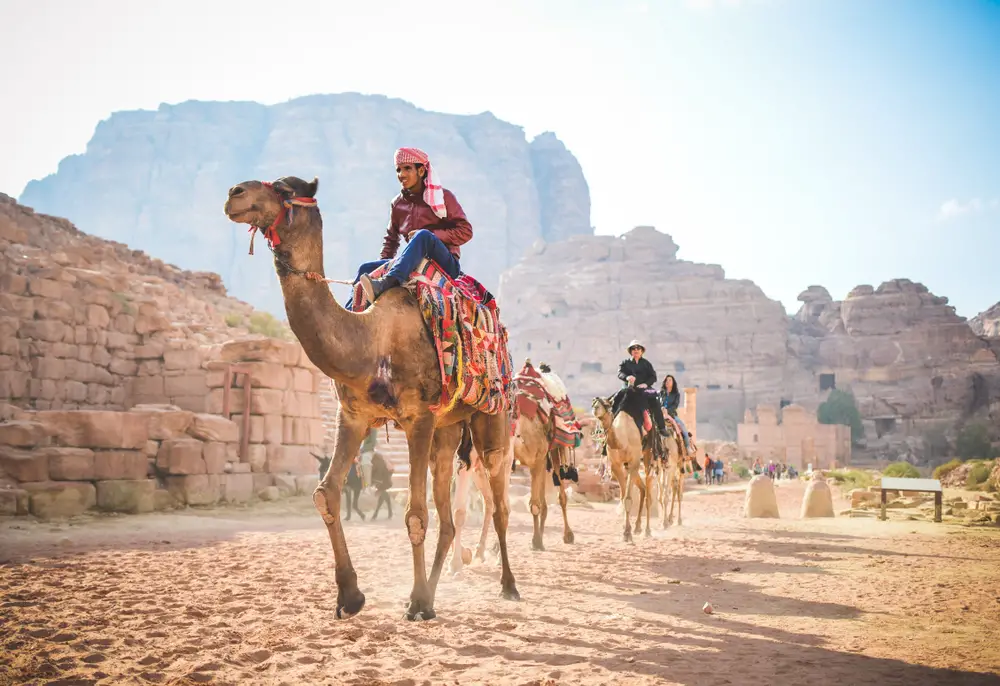 People riding a camel while journeying the desert. 
