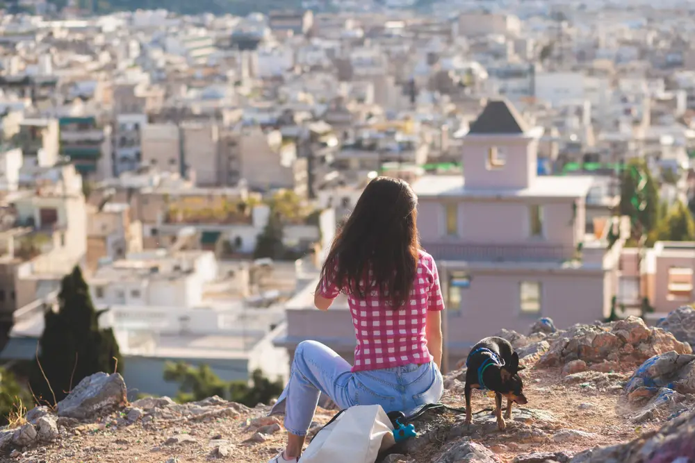 Pictured for a guide titled Is Greece Safe to Visit, a woman sits on a rock looking at Exarcheia, one of the least safe areas to visit on the islands