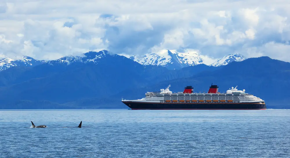 Όμορφη φωτογραφία ενός κρουαζιερόπλοιου στην Αλάσκα με 2 φάλαινες όρκας να παραβιάζουν το νερό και το βουνό στο βάθος για μια λίστα με τις καλύτερες διακοπές all inclusive χωρίς διαβατήριο