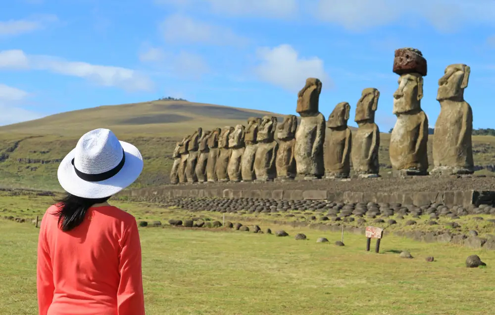 A woman wearing white hat can be seen staring at the humanoid statues from a distance. 