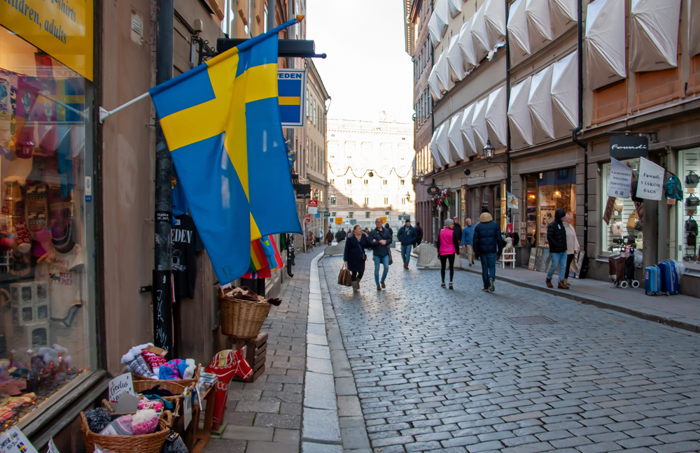 Φωτογραφία ανθρώπων που περπατούν στο δρόμο στη Στοκχόλμη, με έναν δρόμο από τούβλα στη μέση και ιστορικά και μοντέρνα κτίρια εκατέρωθεν του δρόμου