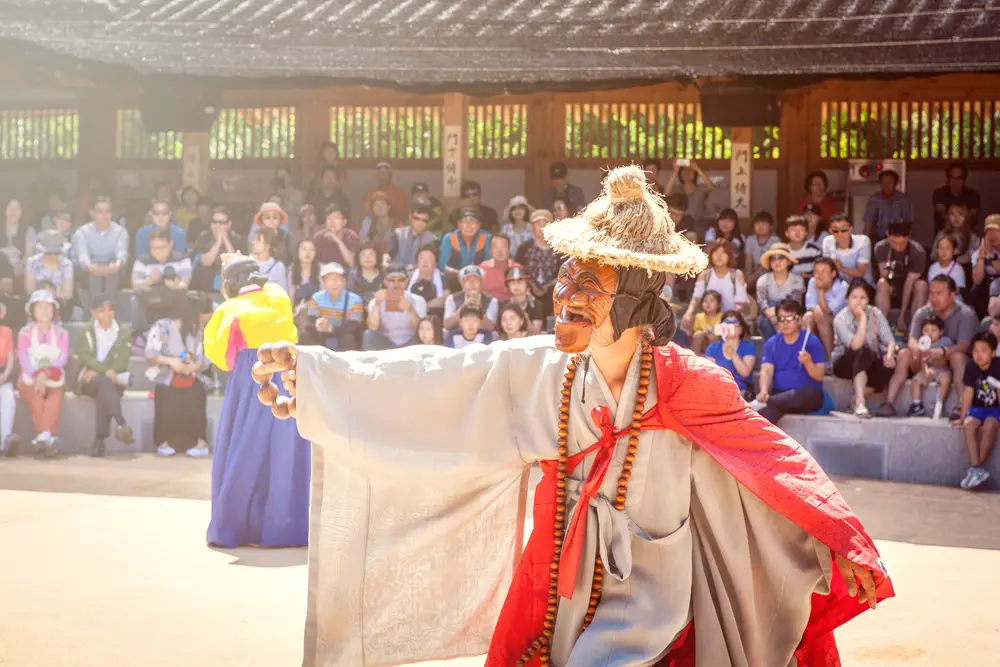 Οι τουρίστες ανενόχλητοι παρακολουθούσαν μια παραδοσιακή ασιατική παράσταση όπου ένας καλλιτέχνης βλέπει να φοράει μάσκα και καπέλο σαν χορό.