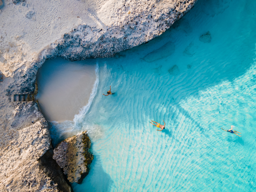 Αεροφωτογραφία σε ένα ζευγάρι που κολυμπά σε μια πεντακάθαρη παραλία με βραχώδη ακτή. 