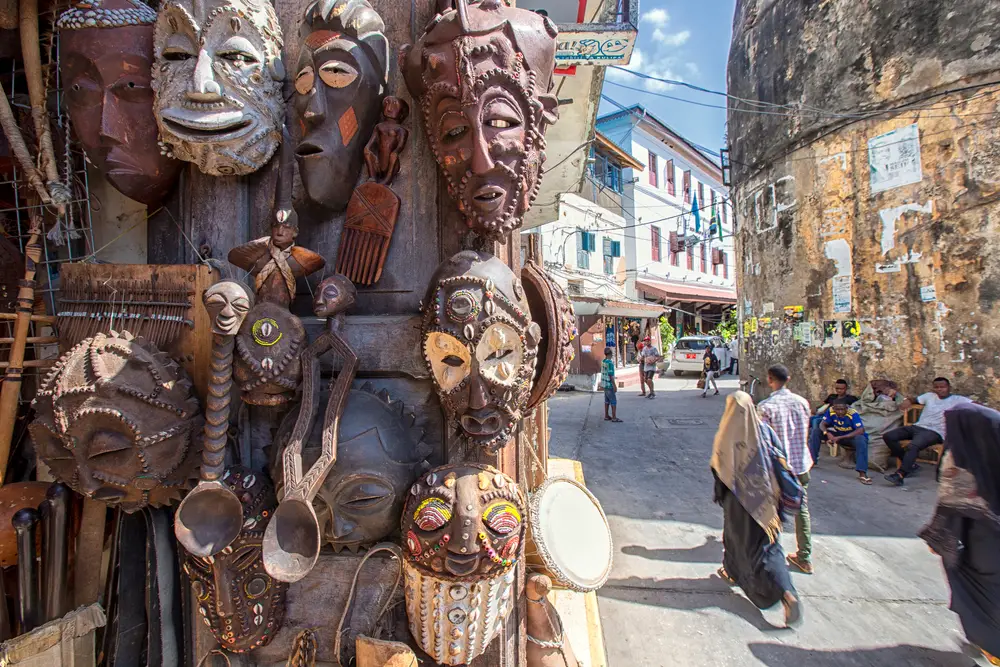 Indigenous masks made of wood displayed on the streets, and people can be seen walking on the street. 