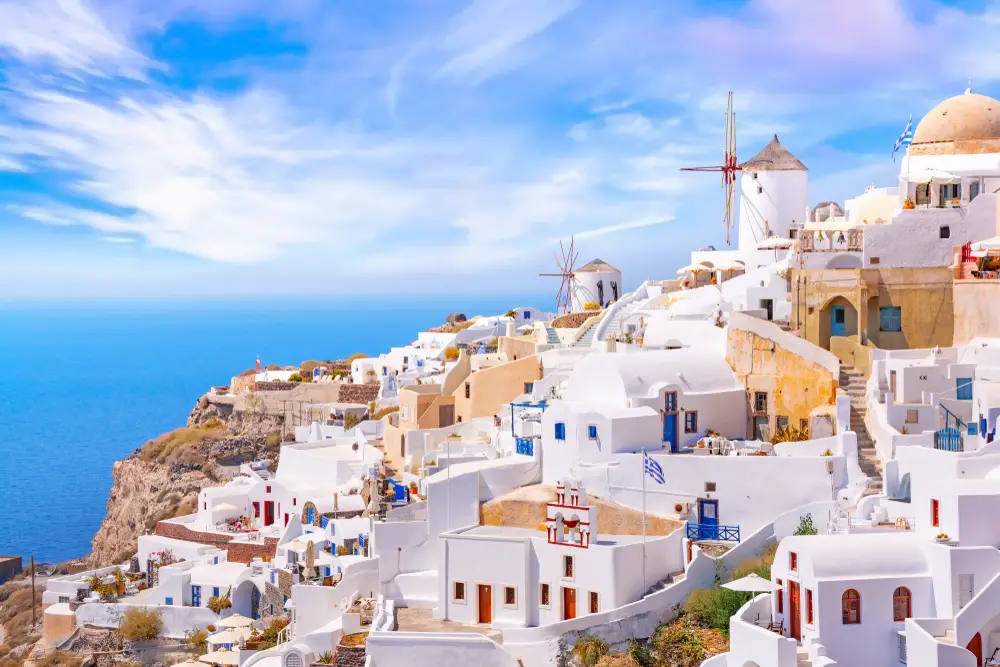 Scenic view of Oia village on Santorini during the daytime with a windmill and buildings on the cliffside for a list of the best party islands in Greece