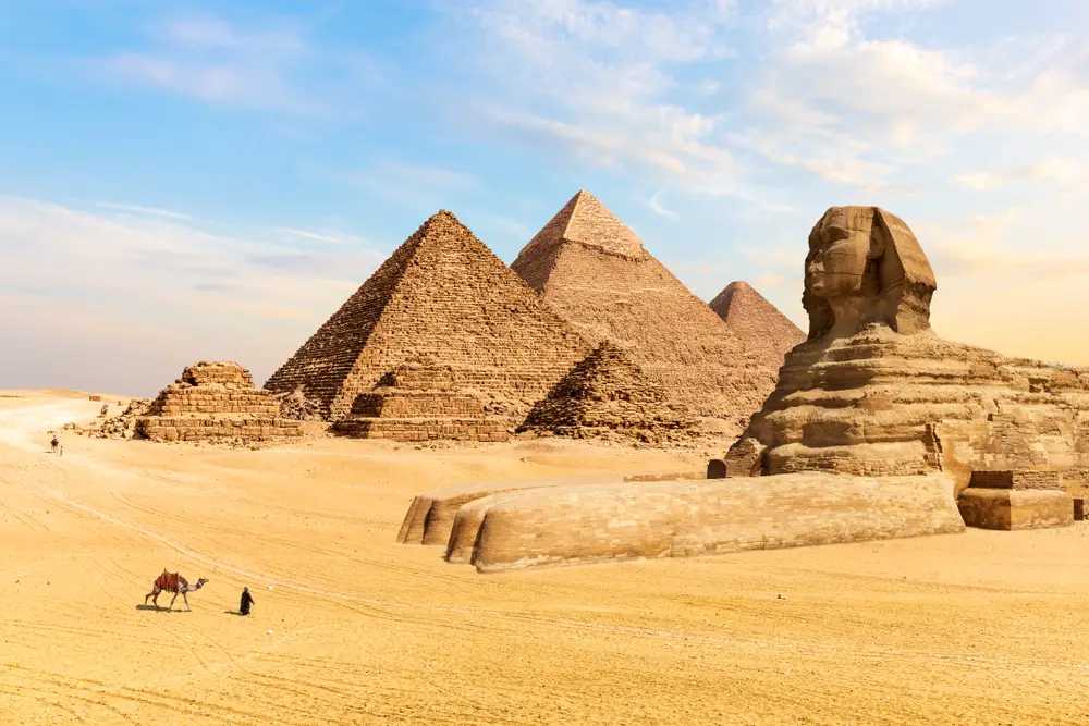 The ever famous pyramid and sphinx in the Egyptian desert, and a man with his camel can be seen walking towards them.