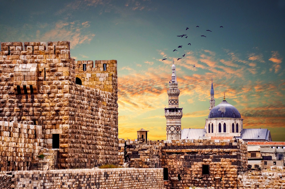 Umayyad Mosque in Syria shown at dusk with birds in flight for a section answering is Syria safe to visit?