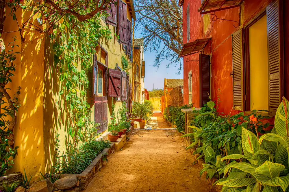 Picturesque street on Goree Island with its orange and red buildings and dirt street in the middle of the homes and a light blue sky overhead, as pictured during the best time to visit Senegal