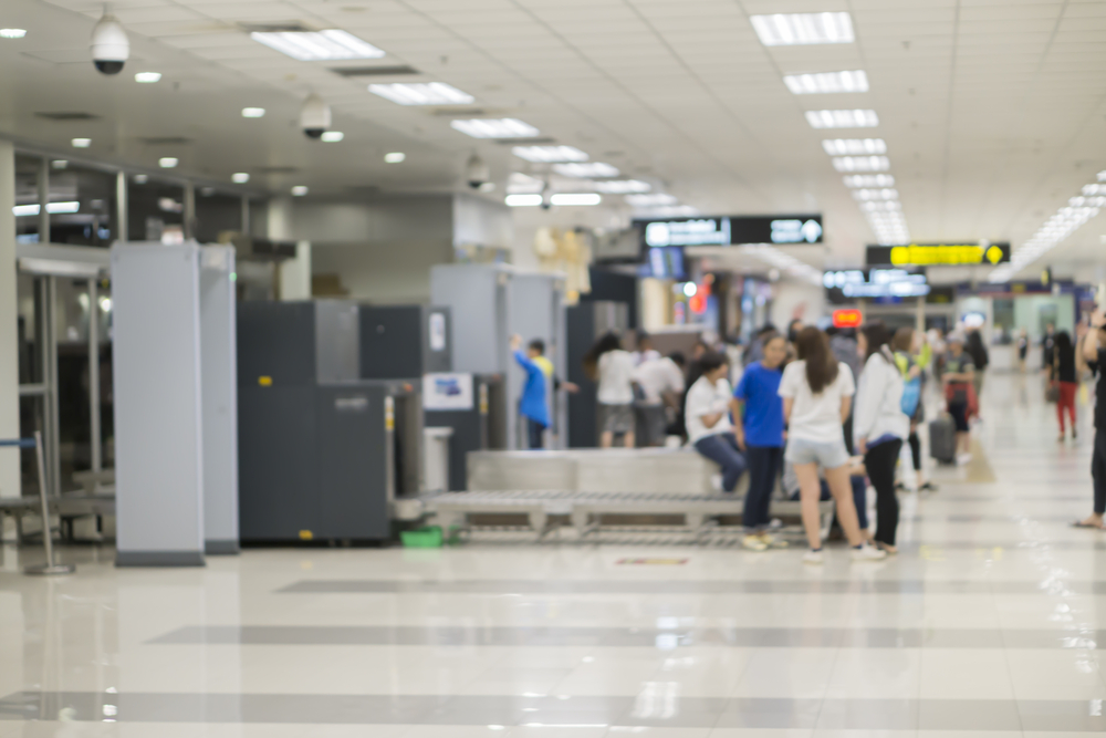 TSA security checkpoint shown blurred out in an airport with passengers waiting in line for a carry on liquid guide