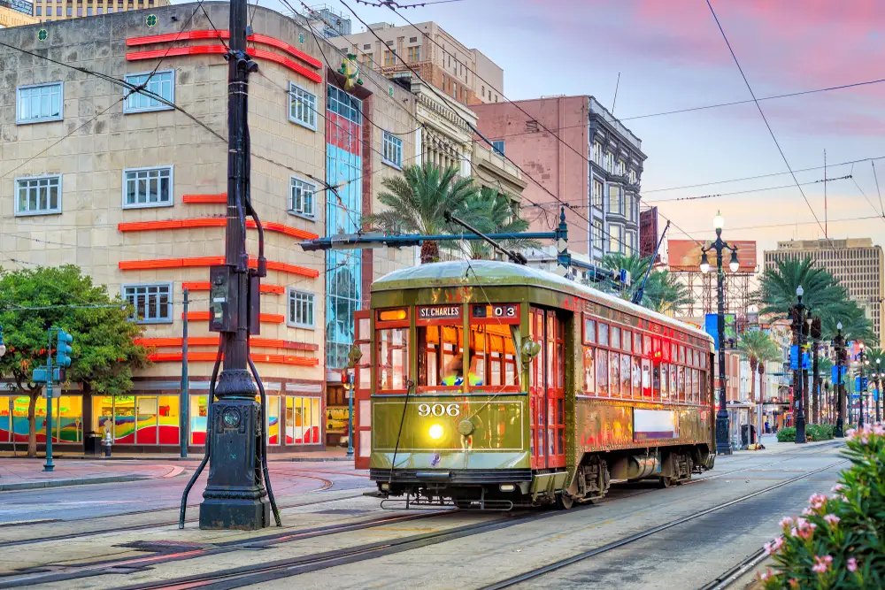 Streetcar in downtown New Orleans pictured for a guide on the average cost of a trip to the city with old-time light poles and buildings on either side of the scene