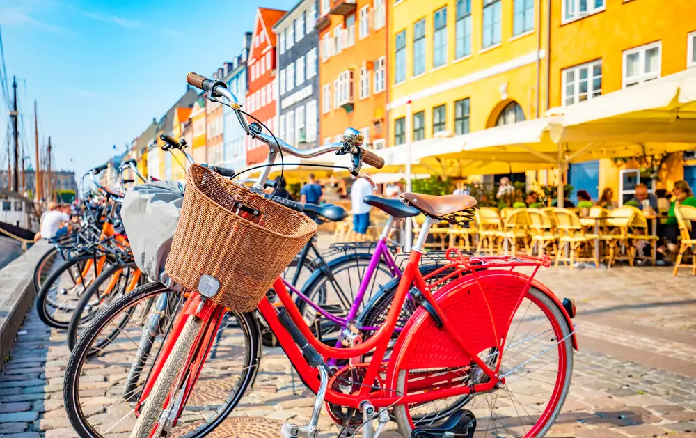 Bicycles parked beside a boardwalk where vibrant structures and restaurants can be seen in background. 