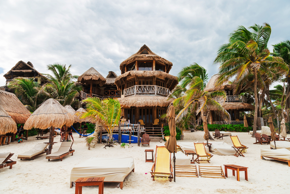Ένα εγγενές ξενοδοχείο στην παραλία με ψάθινες στέγες και μερικές ξαπλώστρες στην ακτή κατά τη διάρκεια μιας συννεφιασμένης ημέρας. 