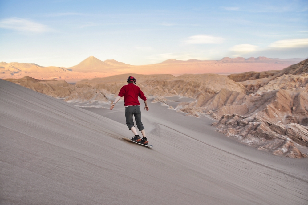 Ένας άντρας που φοράει κόκκινο γλιστράει ομαλά στην άμμο της ερήμου ενώ επιβιβάζεται στην άμμο. 