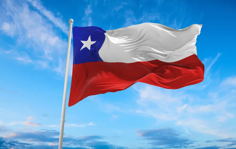 Chile flag waving together with the wind and in background is a little cloudy sky. 