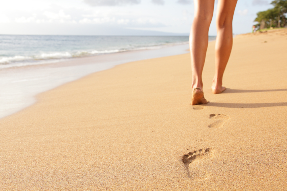 Μια γυναίκα που περπατά στην ακτή αφήνοντας ίχνη στην άμμο.