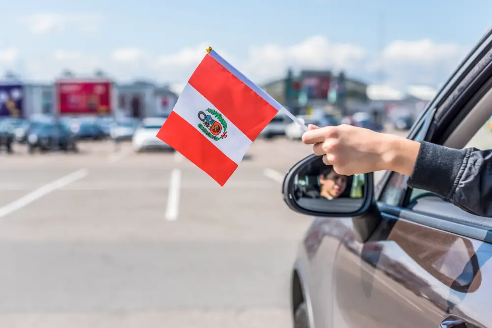 Ένα άτομο που κρατά μια σημαία του Περού έξω από ένα παράθυρο αυτοκινήτου ενώ είναι σταθμευμένο.