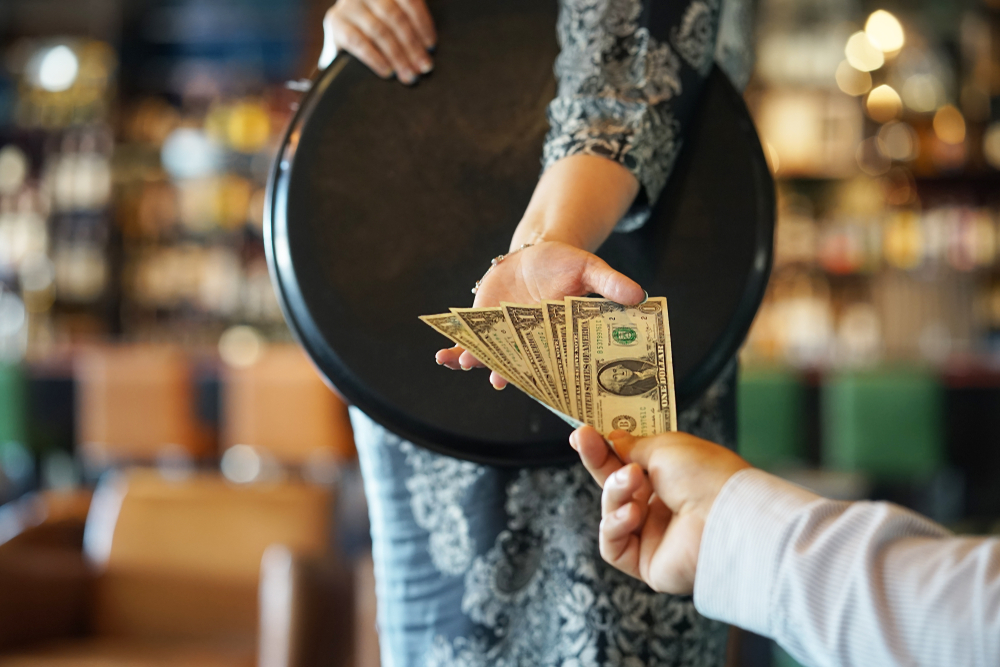 Ένας άντρας δίνει πολλά δολάρια ως φιλοδώρημα σε μια σερβιτόρα που κρατά ένα δίσκο. 