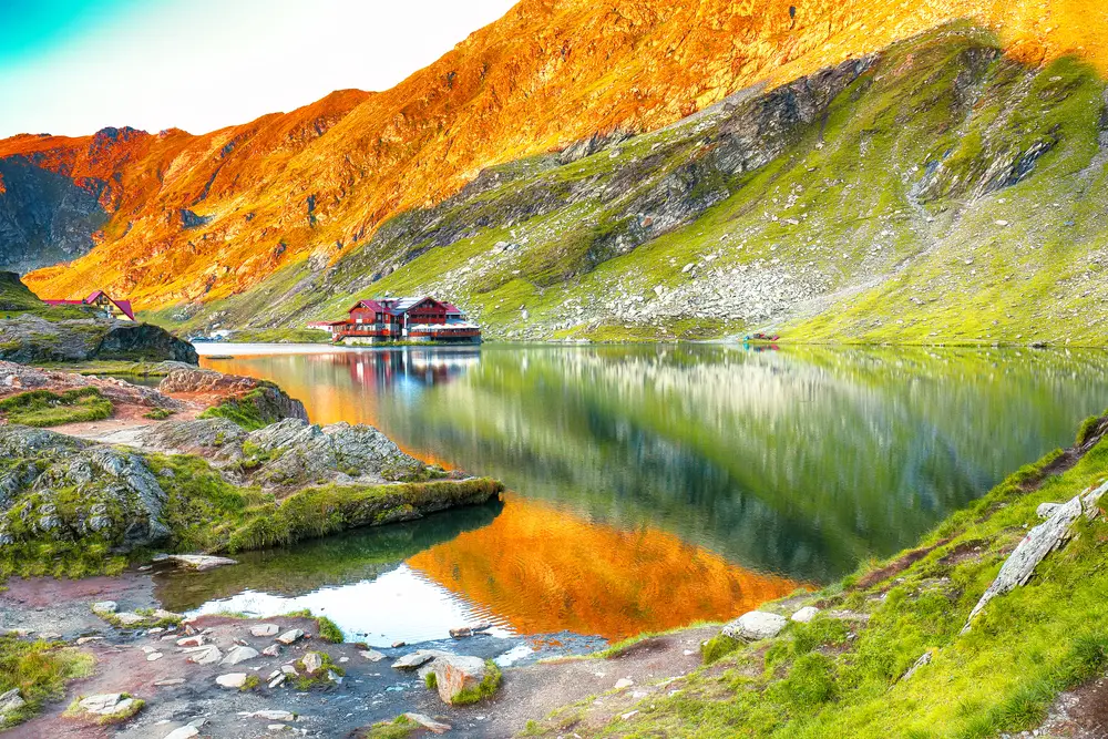 Ένα σπίτι δίπλα σε μια λίμνη που περιβάλλεται από βουνά. 