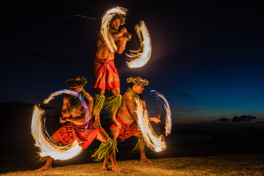 Τρεις άντρες ταχυδακτυλουργούν με πυροσβεστικά ρόπαλα κατά τη διάρκεια μιας βραδινής γιορτής luau στη Χαβάη για ένα κομμάτι που συζητά ποια γλώσσα μιλούν στη Χαβάη;