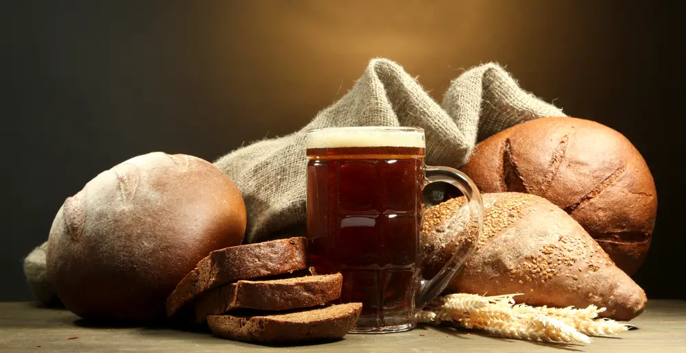A mug of beer paired with piece of bread with barley grain and sackcloth. 