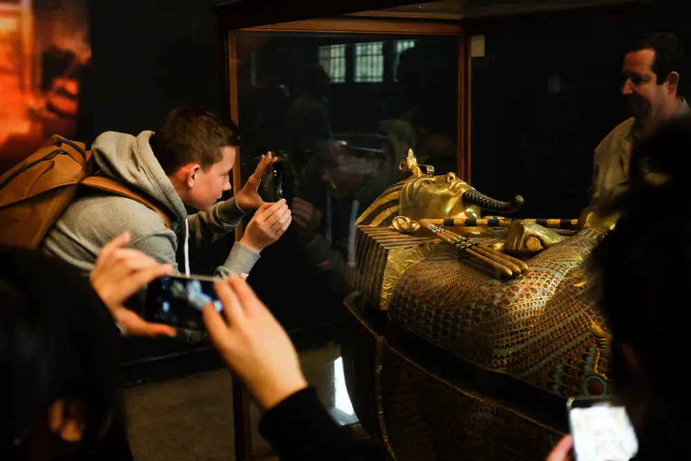 People taking pictures of a preserved pharaoh's tomb at a museum.