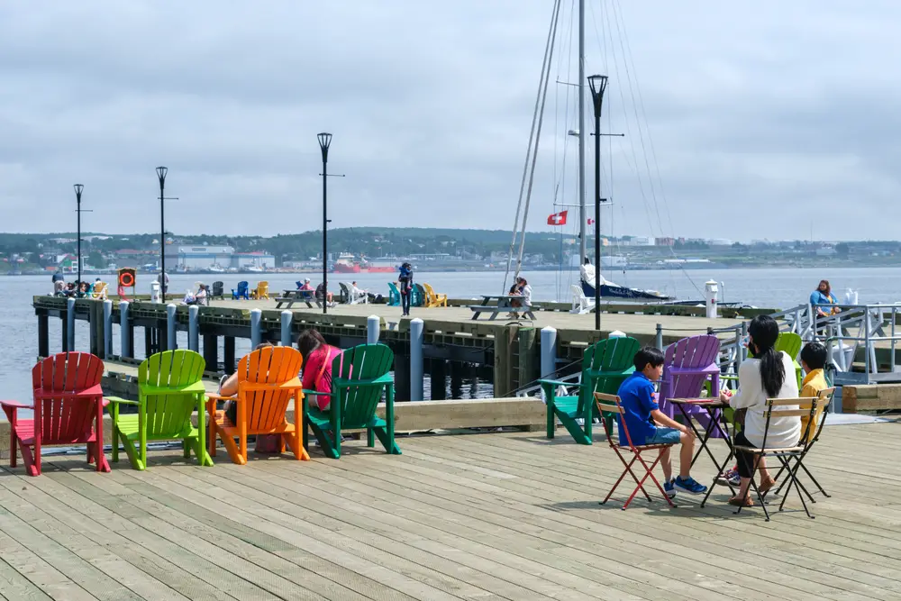 A mother with his two kids enjoying a lunch at a harbor boardwalk with several other people on the dock at an afternoon. 