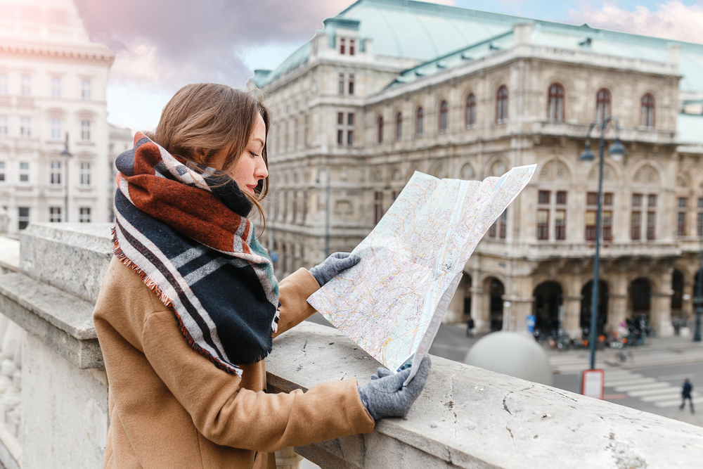 Μια γυναίκα που φορά κασκόλ, παλτό και γάντια κρατώντας έναν χάρτη μιας πόλης.