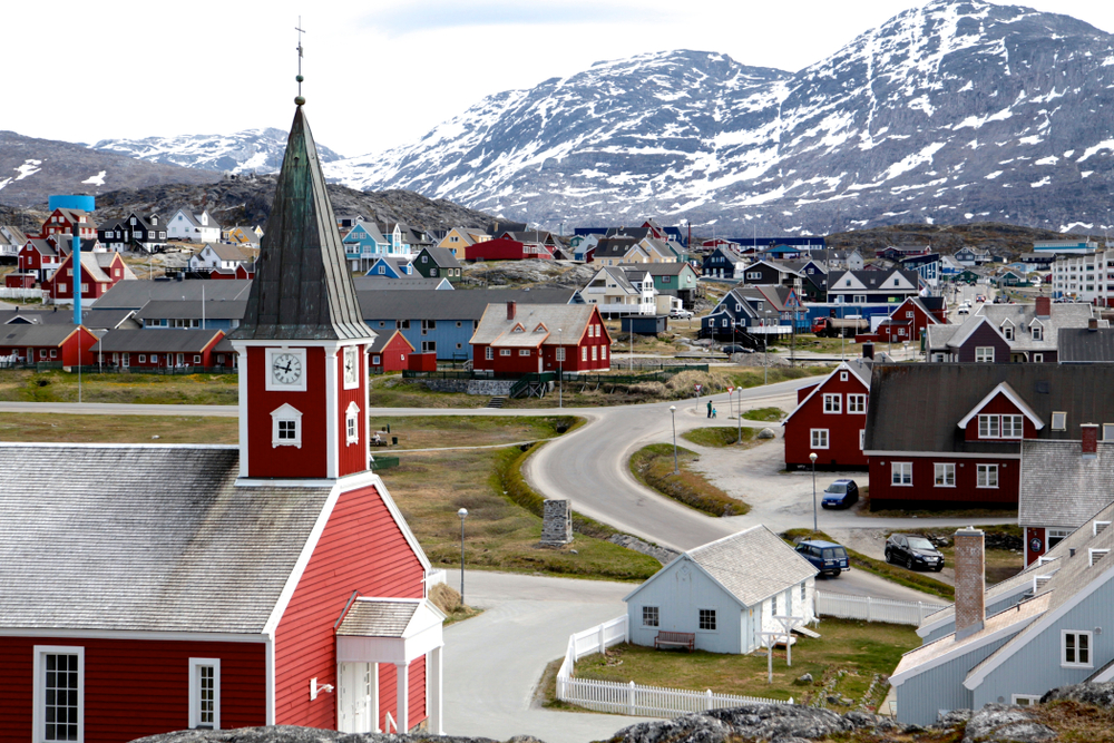A less populated town with church and establishments surrounded by icy mountains.