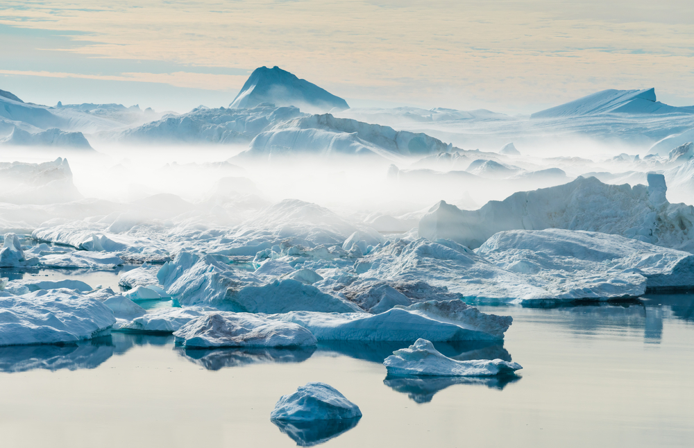 Icebergs can be seen floating in still water where it can be seen smoking from the cold temperature.