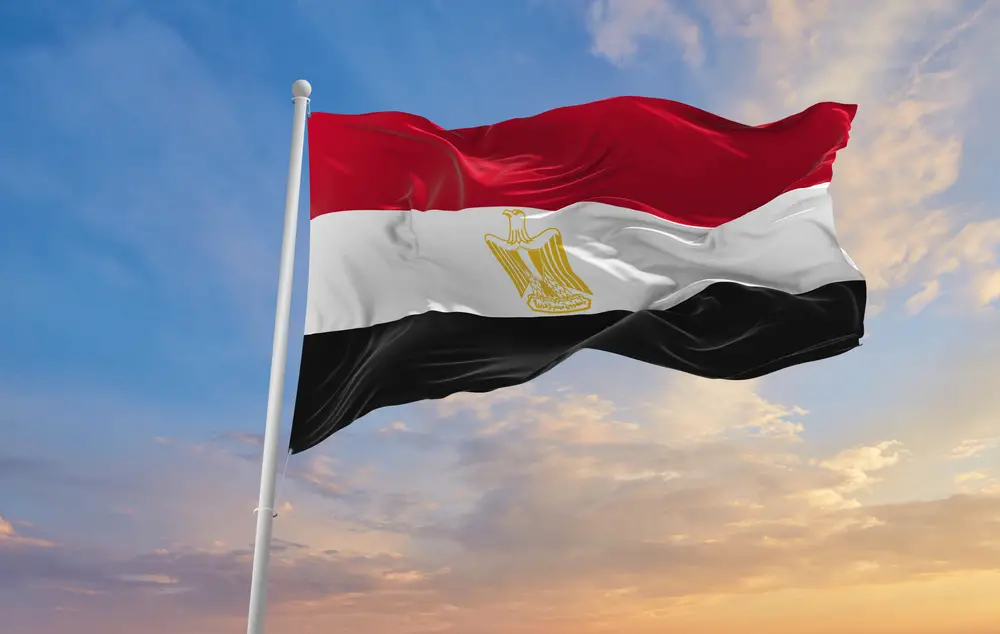 A flag of Egypt on top of a pole waving during a sunset. 