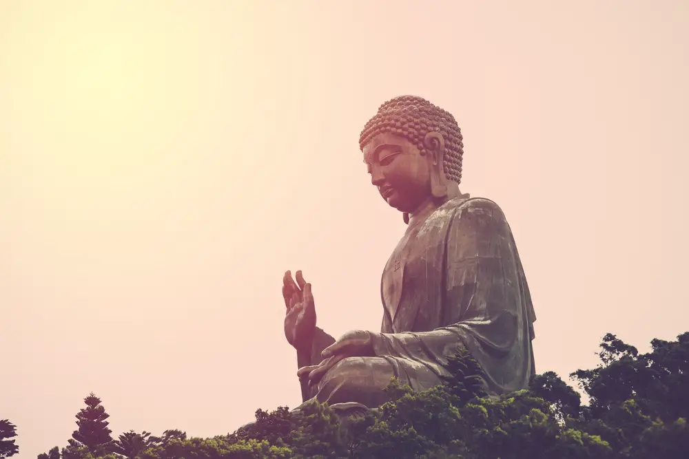 A huge statue of buddha with a gentle face and calm hands during sunset. 