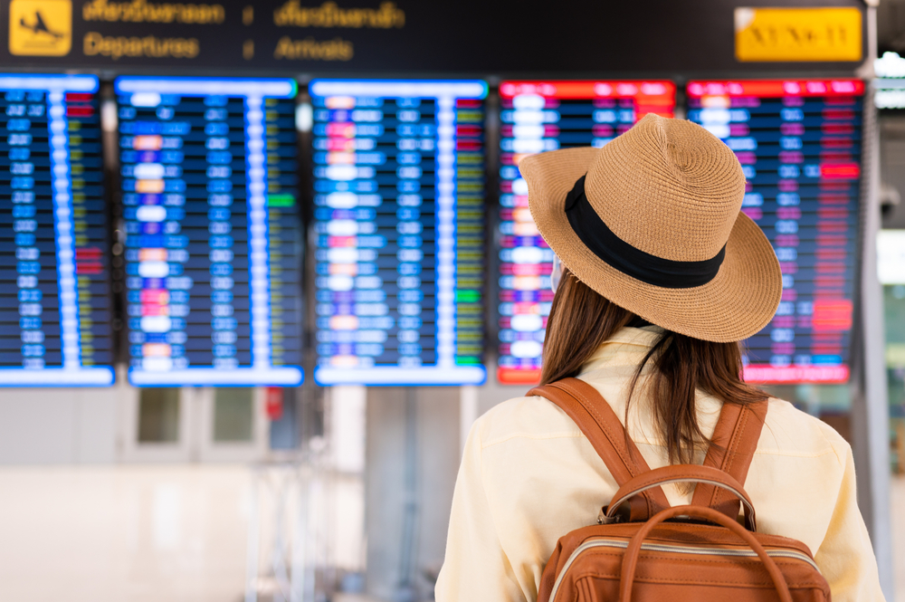 Γυναίκα στέκεται κοιτάζοντας τις ώρες αναχώρησης από το αεροδρόμιο καθώς αναρωτιέται πόσο διαρκεί μια πτήση προς Ταϊλάνδη από τις ΗΠΑ;