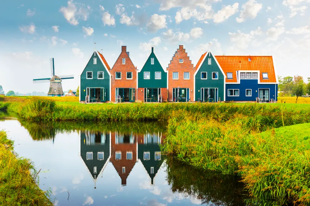 Simple vibrant houses by the side of a small lake with an old windmill at a distance. 