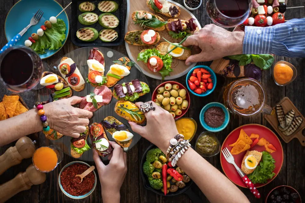 Image looking down at a table filled with tapas plates as hands reach out to share the Spanish food for a comparison guide between it and Portugal