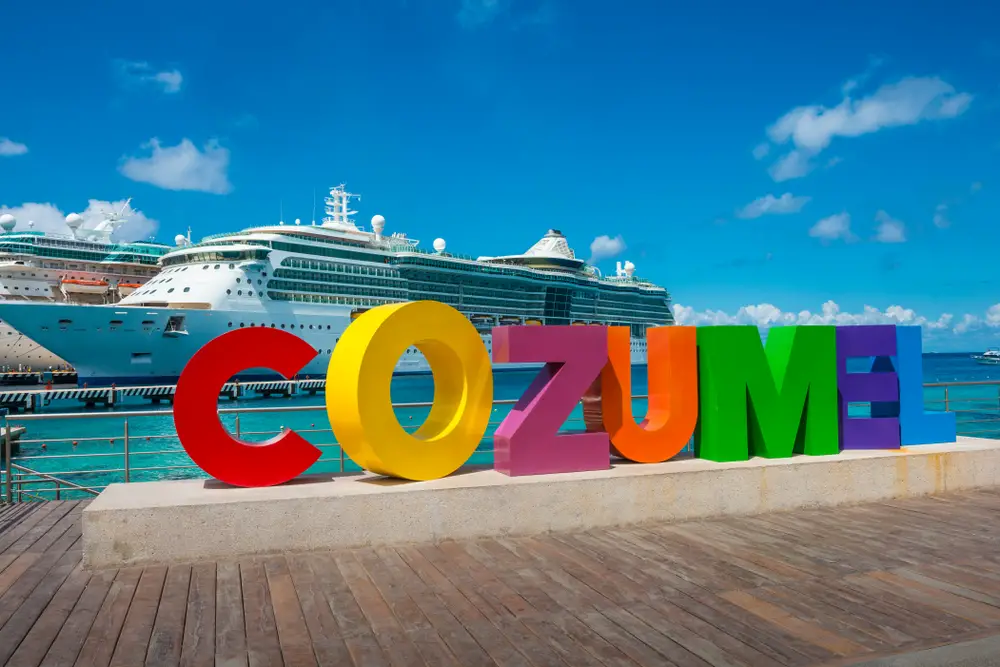 Ένα γράμμα γλυπτό του Cozumel σε ζωηρά χρώματα στο λιμάνι του, όπου φαίνεται ένα κρουαζιερόπλοιο στο βάθος. 