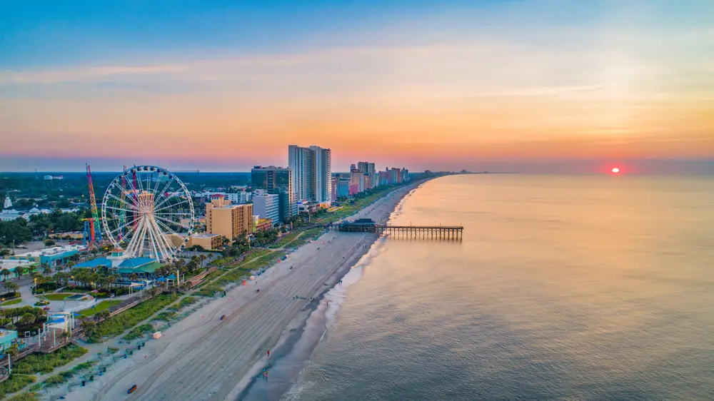 Wide aerial view of Myrtle Beach with the boardwalk and SkyWheel in view at sunrise for a list showing the top summer vacation spots in the US