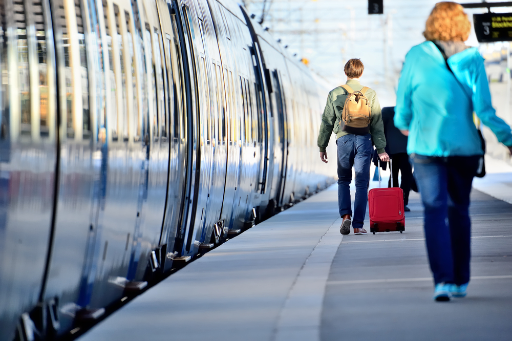 Two people with luggage walk next to the train looking for their car and seats before boarding to travel Europe by train