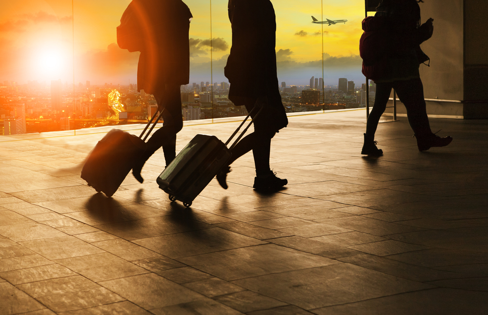 People in business suits walking though the airport in silhouette at sunset with luggage as they embark on bleisure travel