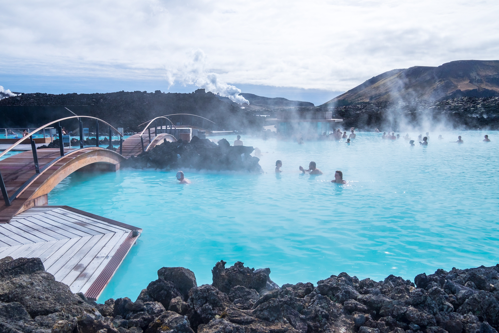 The popular Blue Lagoon geothermal spa in Iceland shown with a bridge and bathers enjoying the warm water for a guide to the length of flights to Iceland from the US